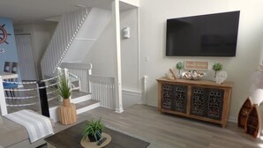A living room with a staircase, a flat-screen TV, a wooden cabinet, and a coffee table. - Charming Family Retreat Near Beach & Boardwalk, 841 Plymouth Place (Ocean City)