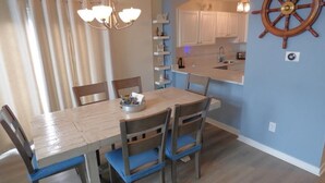 A dining area with a wooden table and chairs, a chandelier, a kitchen with white cabinets, and a ship's wheel decoration on the wall. - Charming Family Retreat Near Beach & Boardwalk, 841 Plymouth Place (Ocean City)