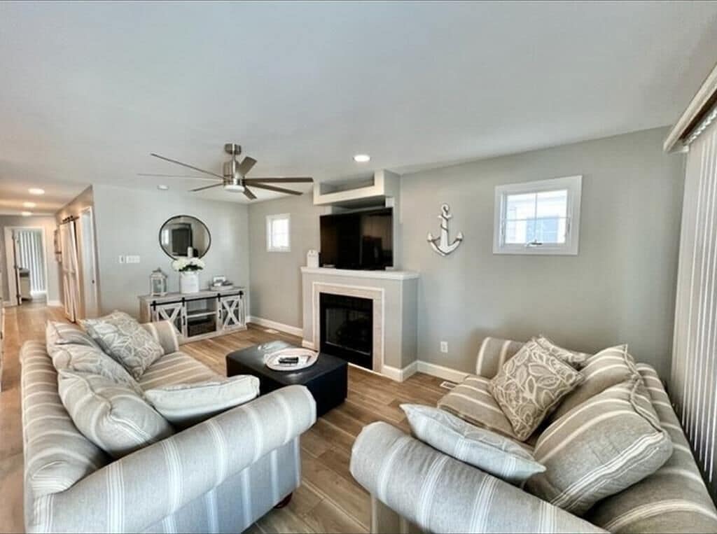 A living room with a fireplace, a ceiling fan, and a large window.