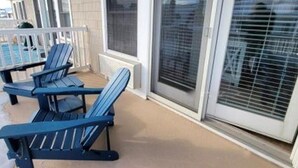 Ein überdachter Außenbereich mit Pool, blauen Adirondack-Stühlen und einem weißen Geländer.