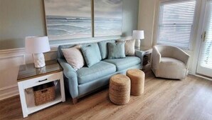 Ein Wohnzimmer mit einem blauen Sofa, zwei Beistelltischen, einer Lampe und einem Sessel.