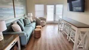Ein Wohnzimmer mit einer Couch, einem Hocker und einem an der Wand befestigten Fernseher.