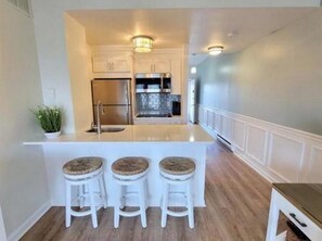 Cozinha com ilha central, banquetas e geladeira.