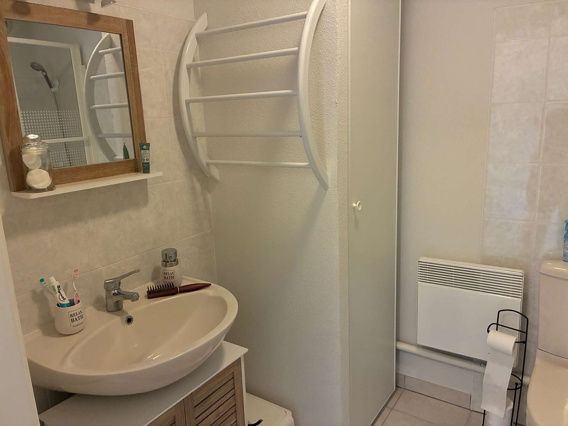 Een badkamer met een wastafel, spiegel, handdoekhouder en douche.