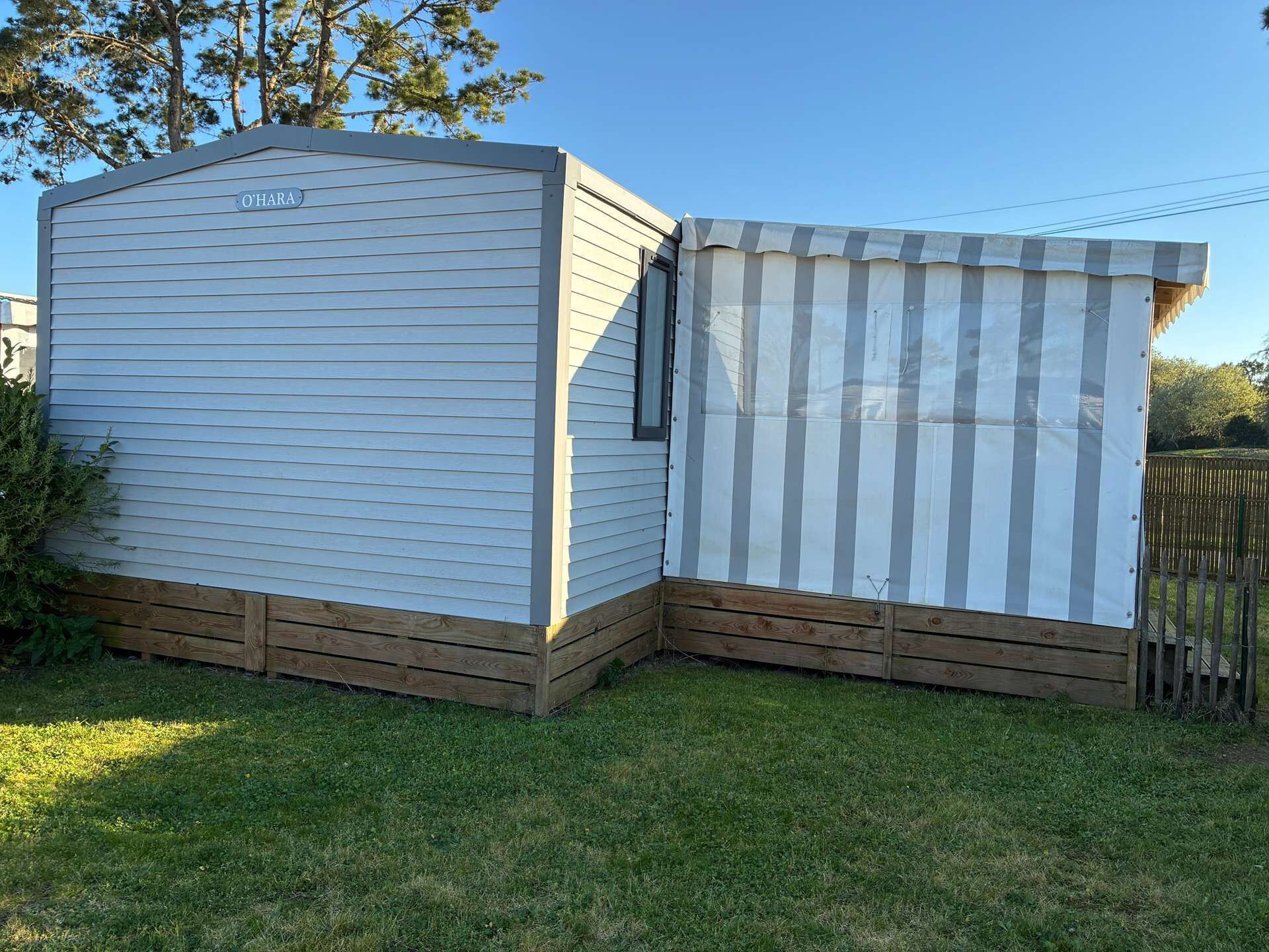 A small, single-story mobile home with a wooden deck and a striped awning.
