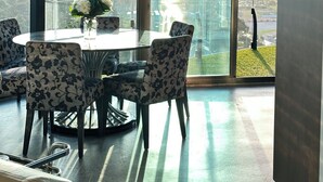 Un espace repas moderne avec une table et des chaises en verre, de grandes fenêtres offrant une vue sur la ville et un vase rempli de fleurs posé sur la table.