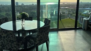 Une pièce située dans un immeuble de grande hauteur, avec une grande fenêtre en verre, une table ronde entourée de chaises et un vase rempli de fleurs.