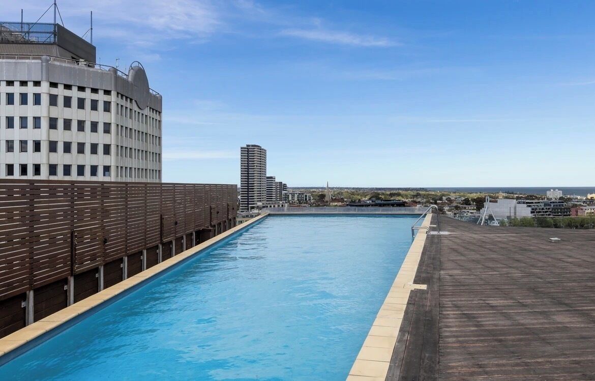 Ein Pool auf dem Dach mit Blick auf eine Stadtlandschaft, darunter ein großes Gebäude und ein hoher Wolkenkratzer.