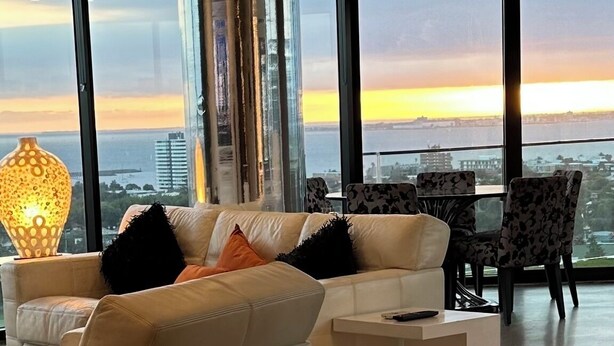 Un salon moderne avec un canapé, une table basse et une lampe. De grandes fenêtres offrent une vue sur le paysage urbain.