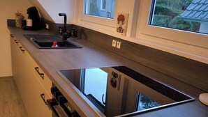 A modern kitchen with a built-in stove, a sink, and a window overlooking a garden. - Vacation apartment Kampić "Hirsch&Heimat" (Rottweil)
