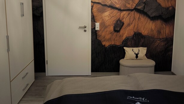 A bedroom with a bed, a wardrobe, a door, a wall with a crack-like pattern, and a chandelier. - Vacation apartment Kampić "Hirsch&Heimat" (Rottweil)