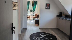 A hallway with a wooden floor, a black rug with text, a door, and a view into a dining area with chairs and a table. - Vacation apartment Kampić "Hirsch&Heimat" (Rottweil)