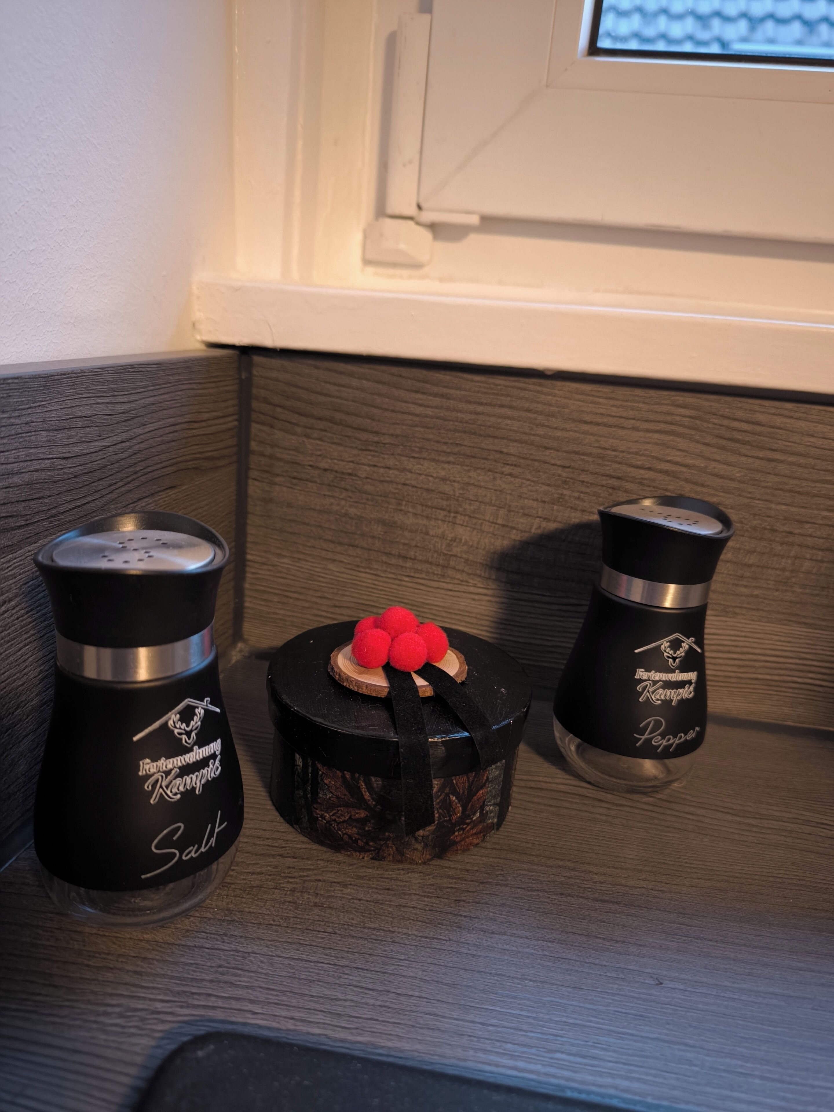 Una estantería con tres recipientes negros, uno decorado con rojo, etiquetado 'Kampfling Pepper'.