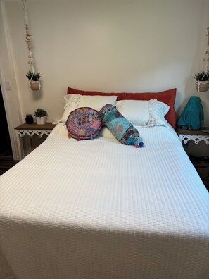 A neatly made bed with a white quilt, a red headboard, and decorative pillows. There are two small potted plants on the nightstand beside the bed.