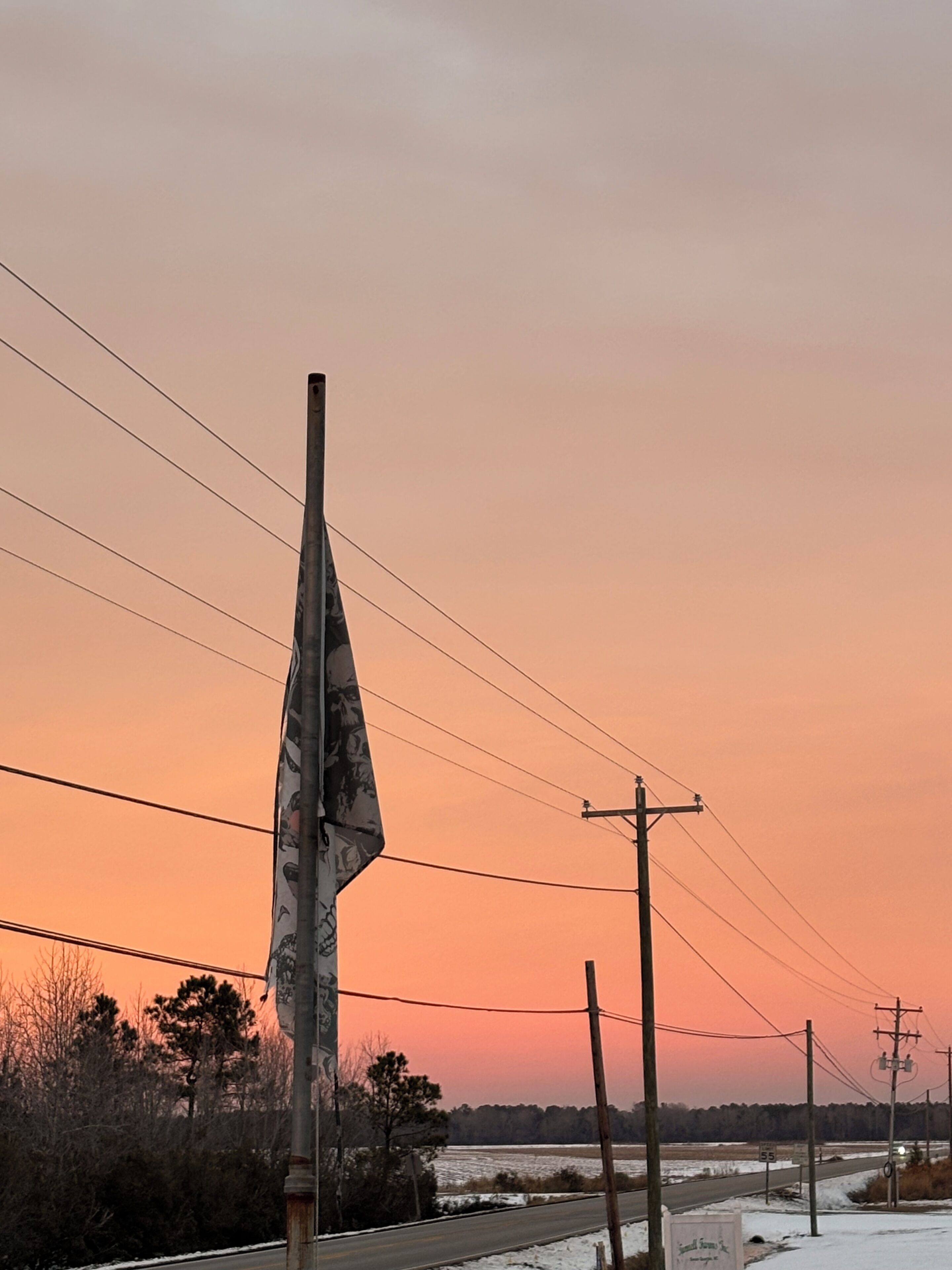 Une route bordée d’un mât de drapeau et de lignes électriques, avec un ciel au coucher du soleil en arrière-plan.