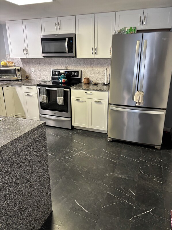 A modern kitchen with white cabinets, a stainless steel refrigerator, a microwave, an oven, and a granite countertop.