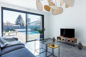 Een moderne woonkamer met een grote televisie, een bank, een bijzettafeltje en uitzicht op een zwembad.
