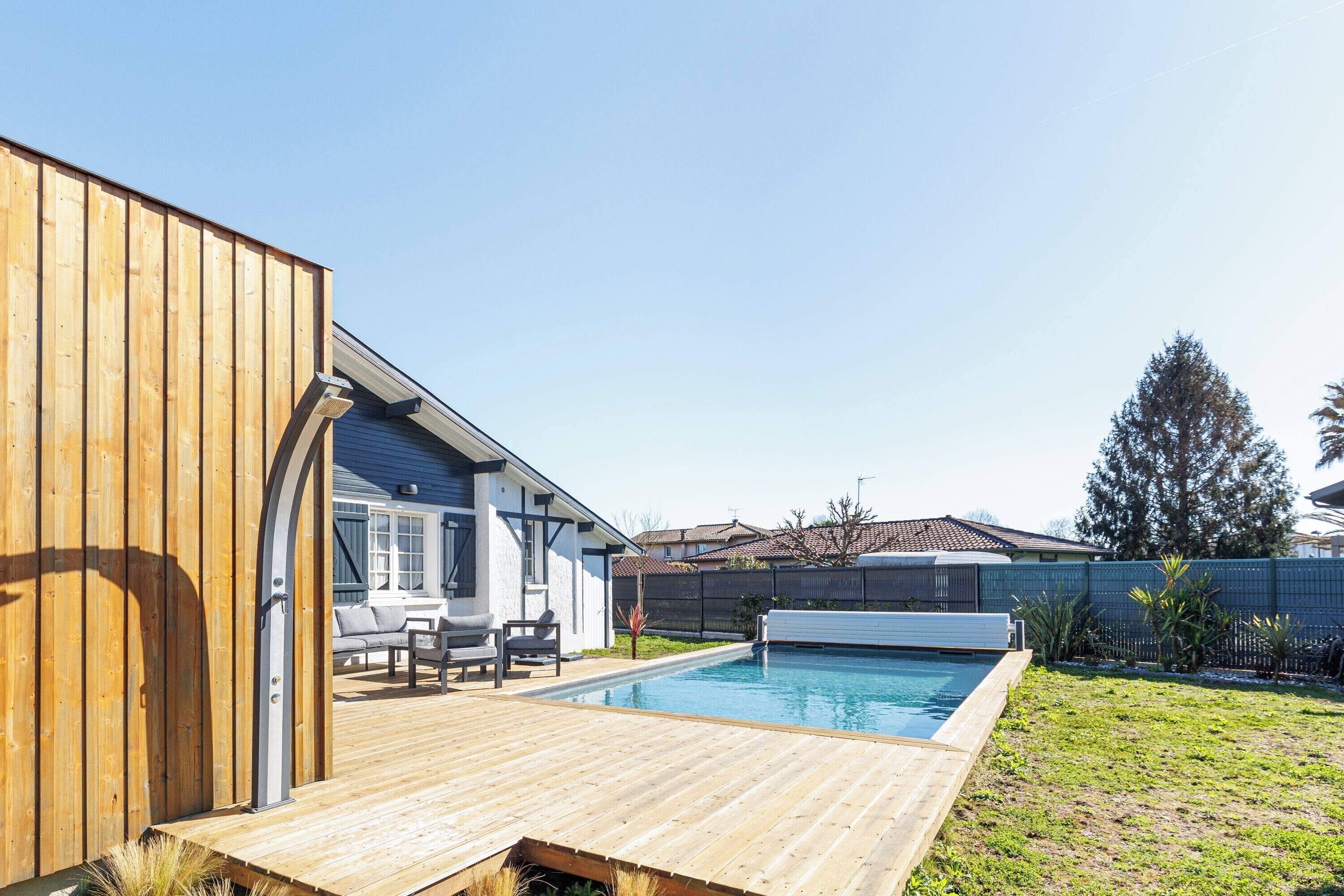 A backyard with a swimming pool, wooden deck, and a patio area with outdoor furniture.