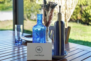 A table with a blue glass vase, a striped bottle, a glass, and a sign with the logo 'wk welkeys'. - Villa Blue Pool - Welkeys (Seignosse)