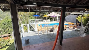 Et overdækket udendørsområde med hængekøje, pool og havemøbler.