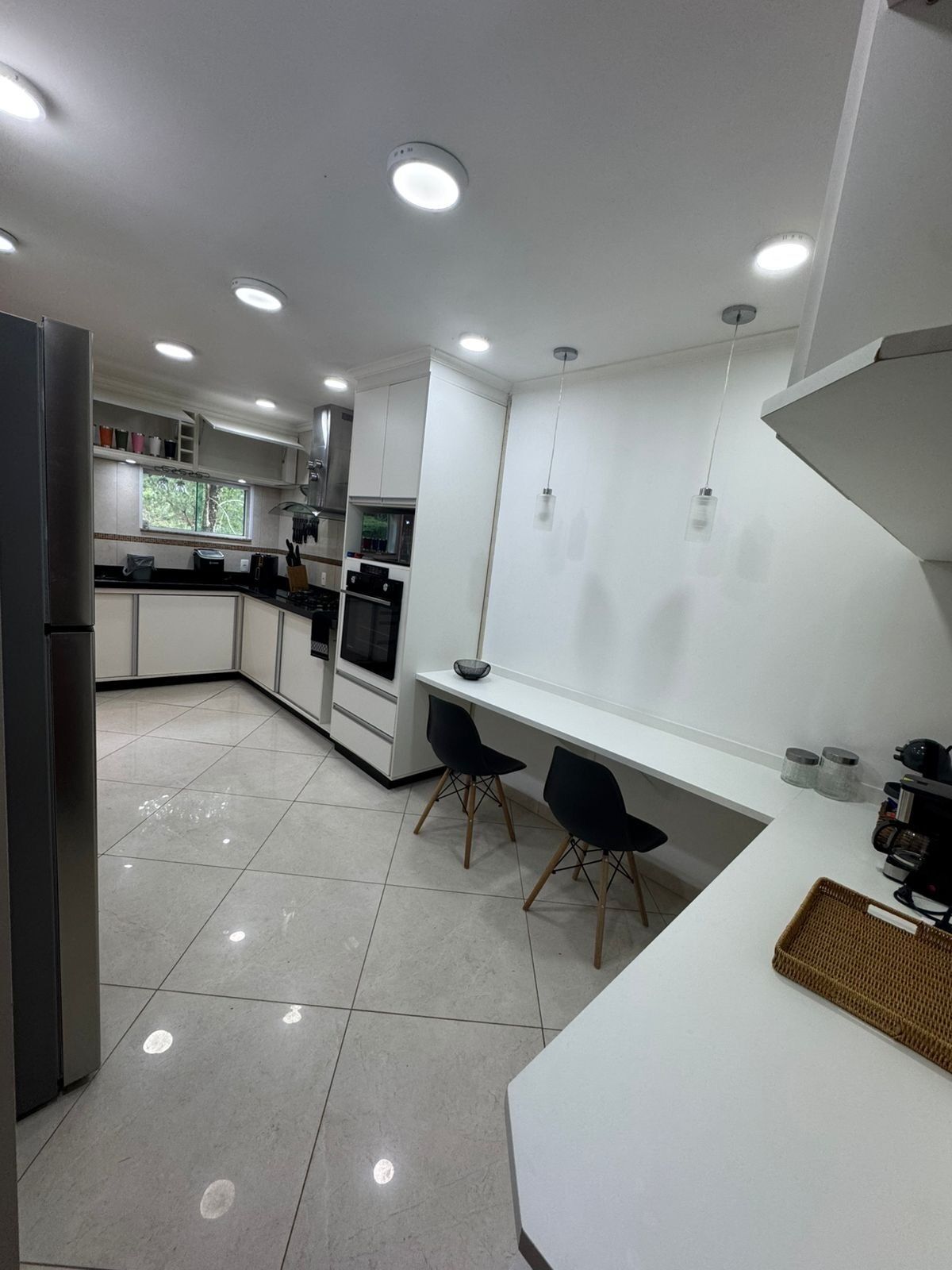 Een moderne keuken met witte kasten, een centraal kookeiland met stoelen en inbouwspots.