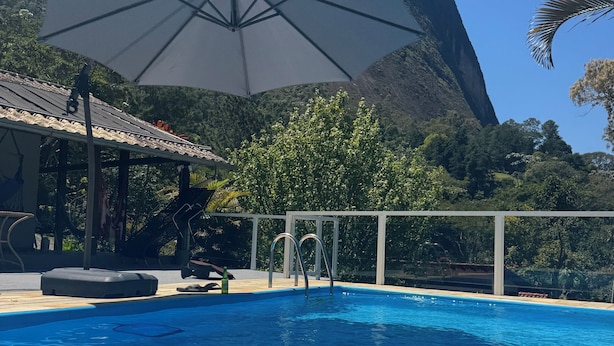 En swimmingpool med et bjerg i baggrunden, et overdækket opholdsområde og en klar himmel.