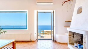 A room with a large window, a door leading to an outdoor terrace, a fireplace, and a radiator. - Lighthouse Villa w Private Pool & 220° Sea View (Faros Armenistis)