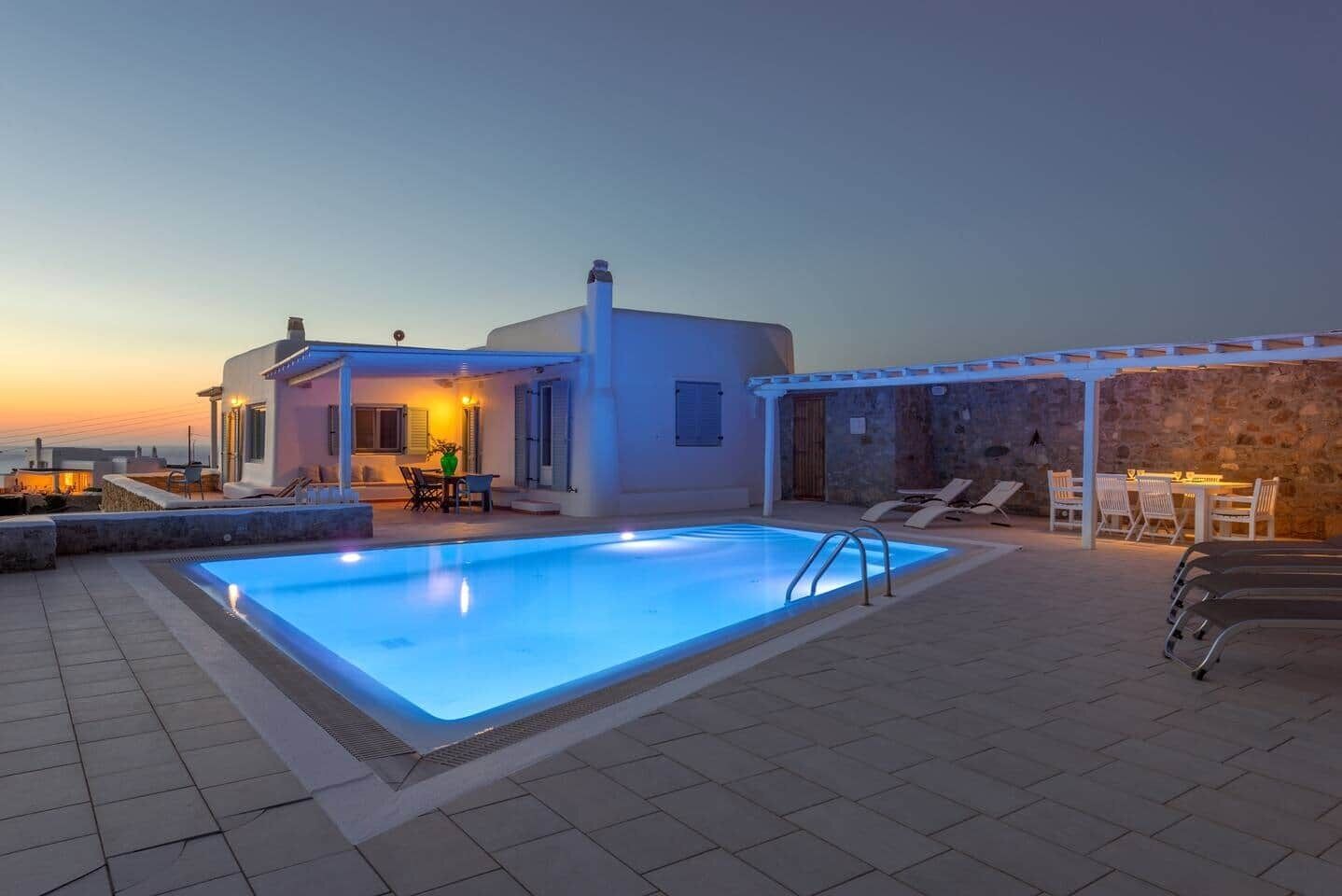 A modern villa with a swimming pool, outdoor seating, and a stone wall.
