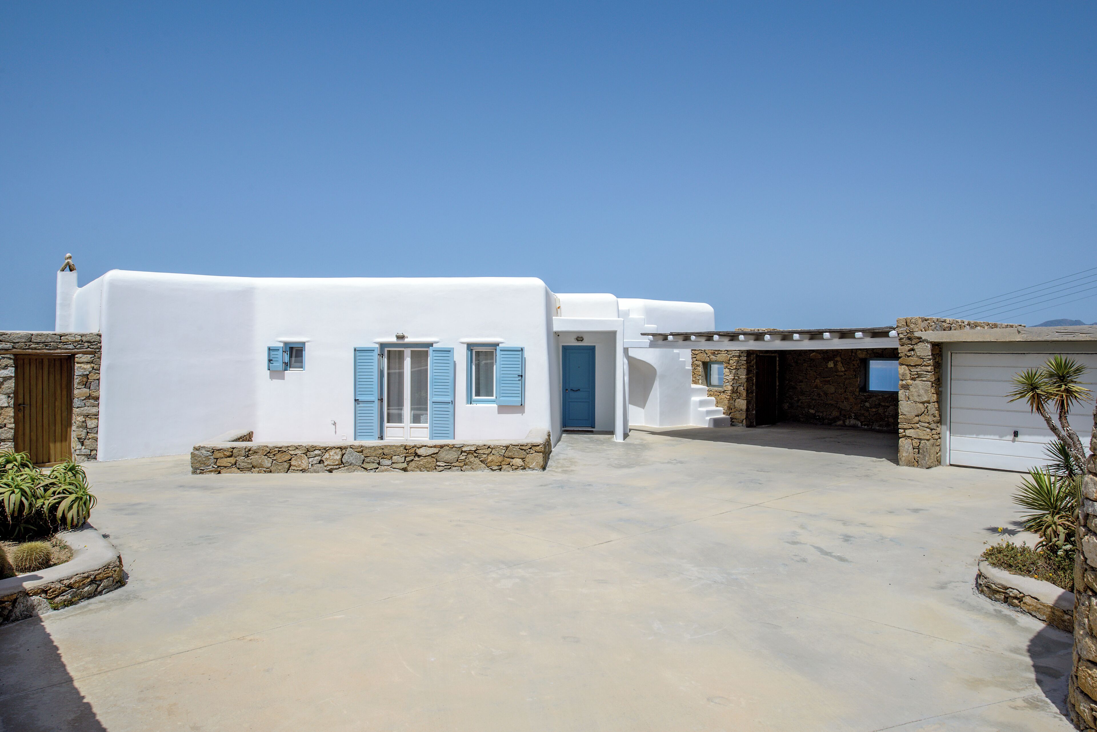 Um edifício branco com toldos azuis, entrada em pedra e garagem.
