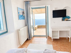 Ein Zimmer mit Bett, Schreibtisch, Fernseher, einem Gemälde und Meerblick.