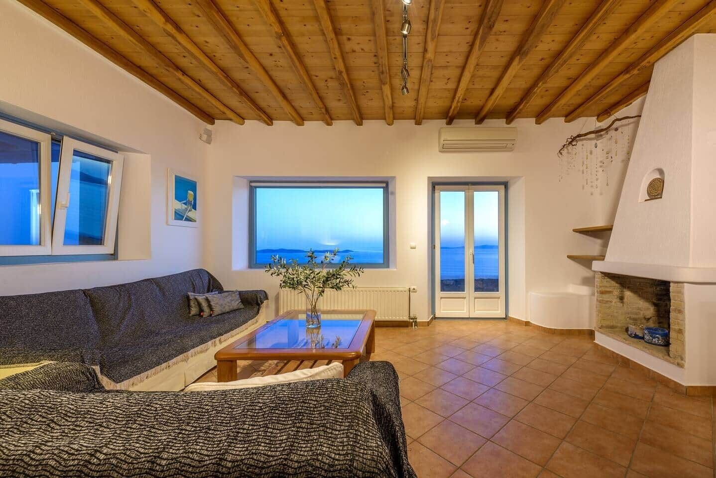 Ein Wohnzimmer mit Holzboden, einer Couch, einem Couchtisch, einem Kamin und Meerblick durch ein Fenster und eine Tür.