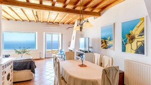 A spacious room with a wooden ceiling, a dining table, chairs, a TV, and artwork on the walls. - Lighthouse Villa w Private Pool & 220° Sea View (Faros Armenistis)