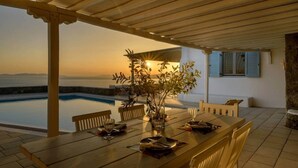 A wooden dining table set for two with a view of the sea at sunset. - Lighthouse Villa w Private Pool & 220° Sea View (Faros Armenistis)