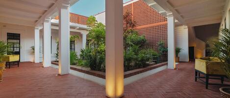 An open courtyard with a herringbone floor, white columns, and potted plants.