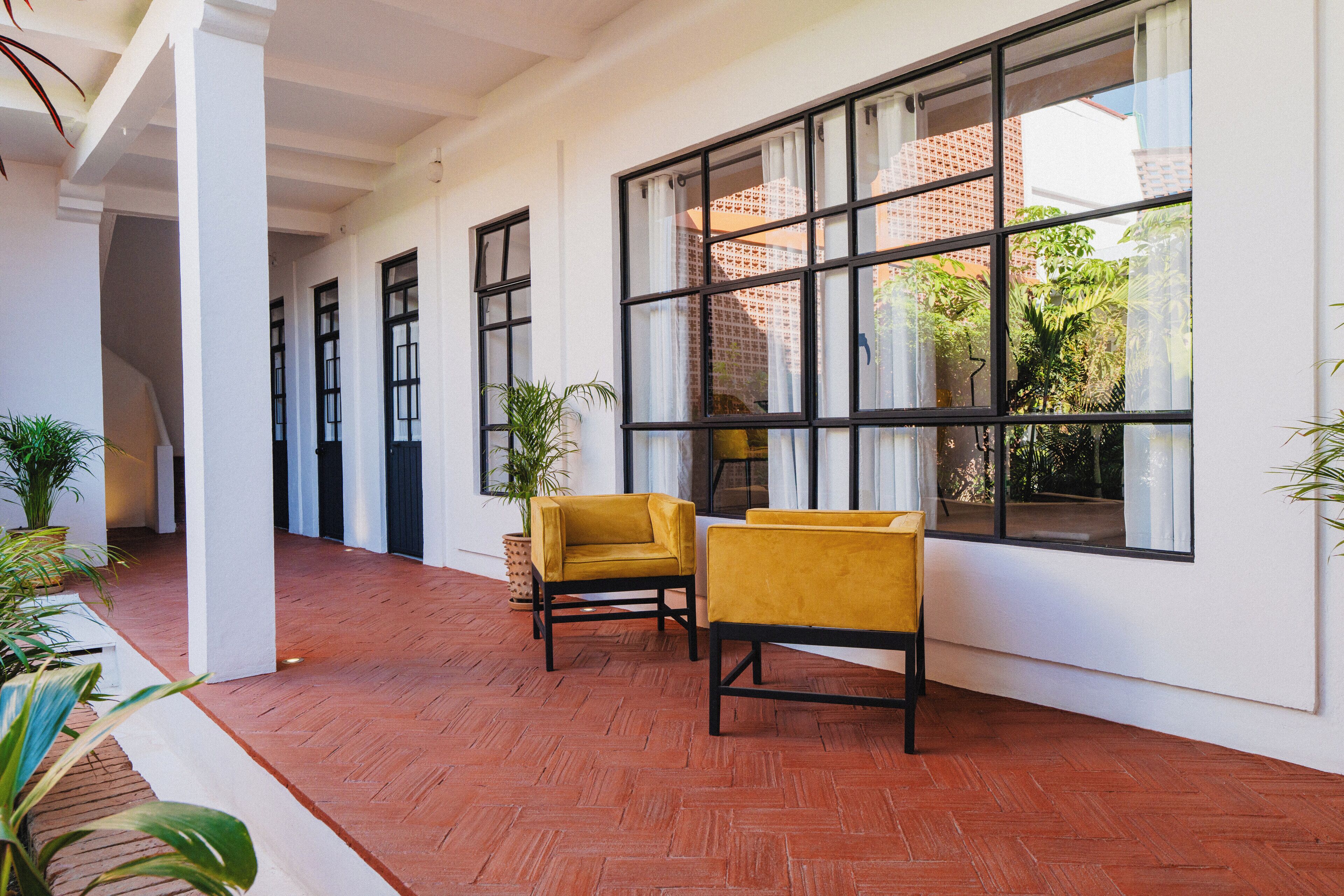 A covered outdoor area with a brick floor, two yellow chairs, and large windows with white curtains.