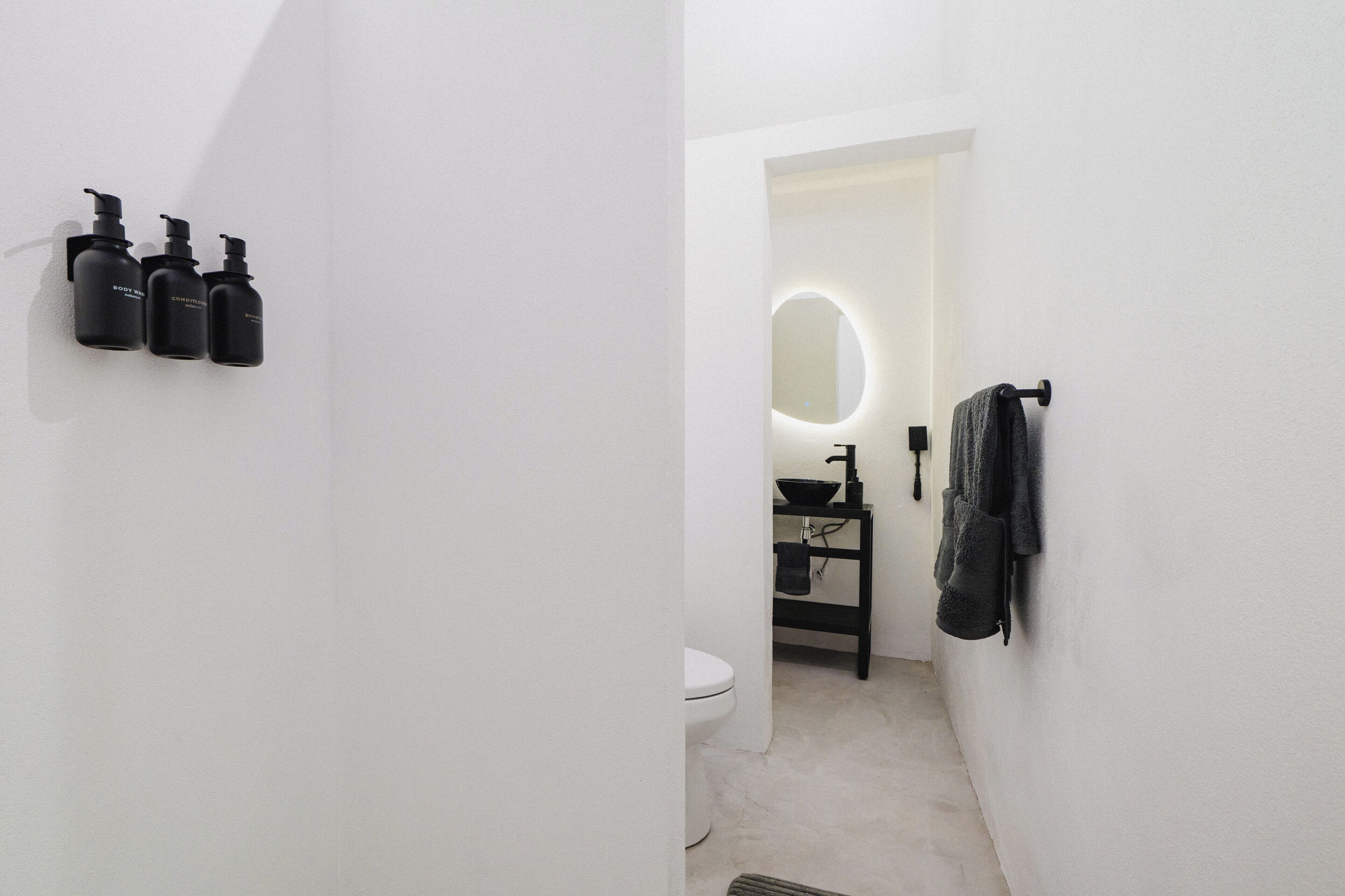 A bathroom with a toilet, sink, and mirror. There are three black bottles on the wall.