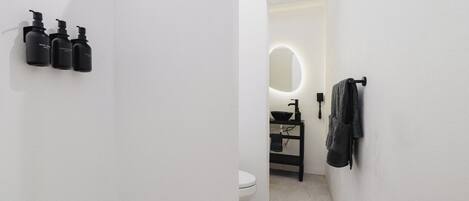 A bathroom with a toilet, sink, and mirror. There are three black bottles on the wall.