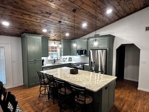 A kitchen with a large island, green cabinets, stainless steel appliances, and pendant lighting. - Edgewater at Lake Greeson – Family Retreat w/ Game Room & Theater (Kirby)