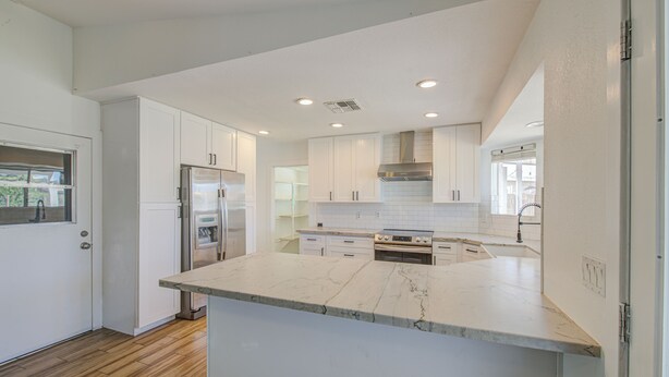 Una cocina moderna con armarios blancos, encimera de mármol y electrodomésticos de acero inoxidable.