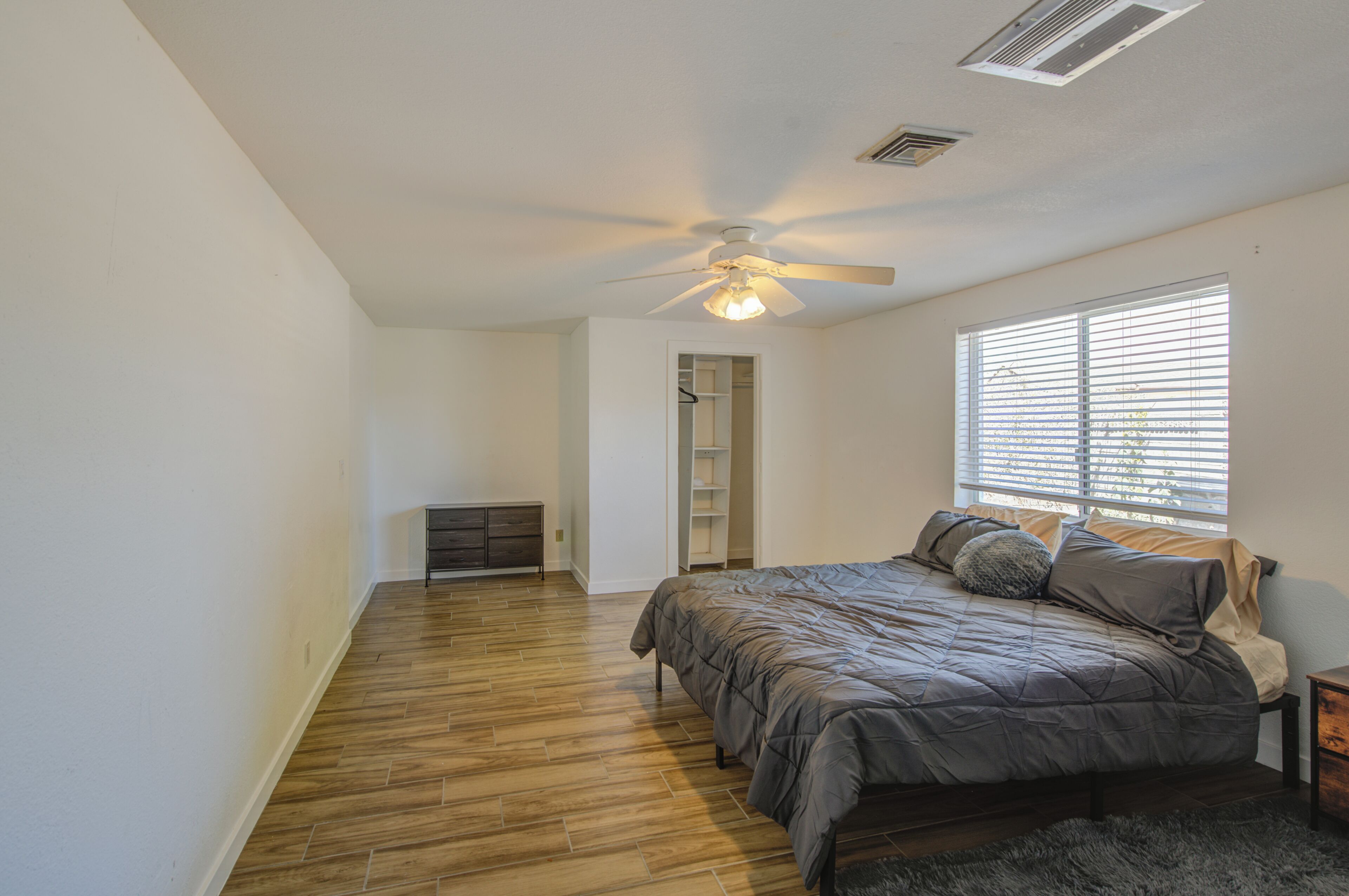 Une chambre à coucher avec un lit, un ventilateur de plafond et une fenêtre avec des stores.