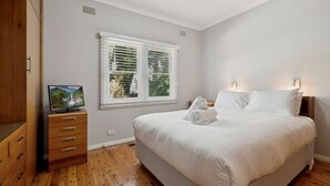 Un dormitorio con una cama, un televisor sobre una cómoda de madera y una ventana con persianas.