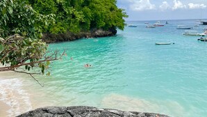 A coastal scene with clear turquoise waters, a rocky shoreline, and a lush green hill. - Thula Lembongan Villa 3 (Lembongan)