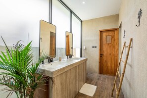 A bathroom with a wooden vanity, a large mirror, and a door. - Thula Lembongan Villa 3 (Lembongan)