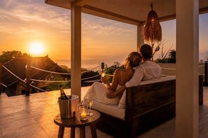 A couple sitting on a wooden bench overlooking a sunset with a bottle of champagne and glasses on a small table. - Thula Lembongan Villa 3 (Lembongan)