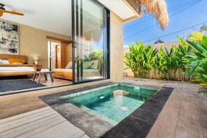 Un dormitorio moderno con puerta de vidrio que da a un balcón, una piscina pequeña y abundante vegetación.
