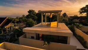 A modern building with a flat roof, a covered outdoor seating area, and a view of a mountainous landscape. - Thula Lembongan Villa 3 (Lembongan)