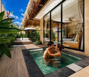 Ein Paar im Pool, im Hintergrund ein modernes Haus und tropische Pflanzen.
