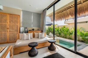 Ein modernes Schlafzimmer mit einem großen Bett, einem kleinen Tisch und Blick auf einen Swimmingpool.