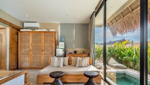 A bedroom with a bed, bedside tables, a wardrobe, a water dispenser, and a view of a pool and tropical plants. - Thula Lembongan Villa 5 (Lembongan)