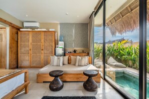 Ein Schlafzimmer mit Bett, Nachttischen, einem Kleiderschrank, einem Wasserspender und Blick auf einen Pool sowie tropische Pflanzen.